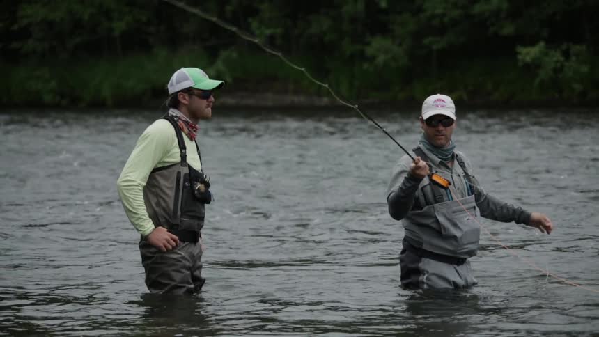 Two men stand fly fishing in a river