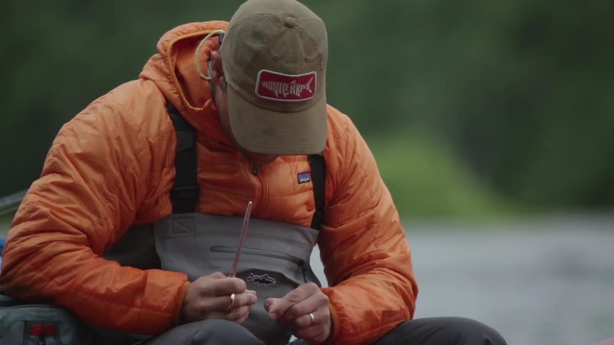 A fisherman wearing waders clips fishing line