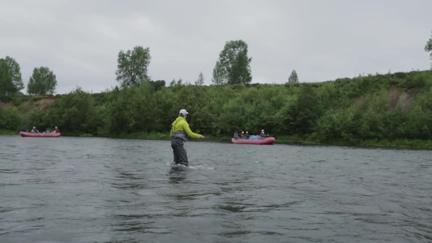 Rafts passing by a man who is fly fishing