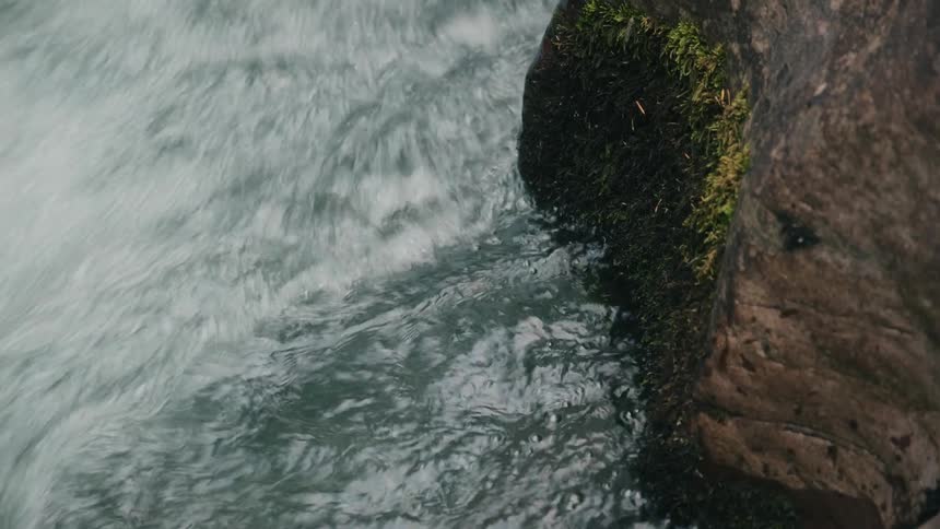 Water from rapids splashing on a rock with moss growing on it