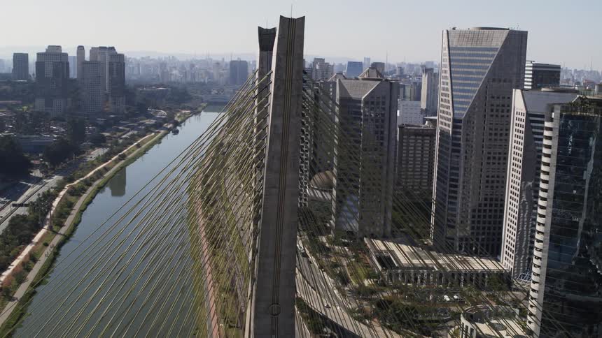 The tower of a suspension bridge spanning a river in a metropolis during the day