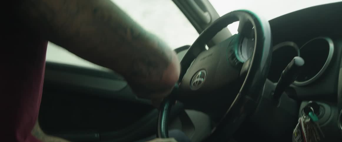 Tattooed man turning the steering wheel of a manual transmission car at daytime