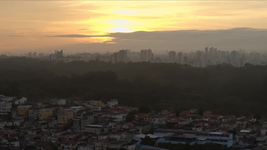 The slums and downtown area of a metropolis separated by tall forested hill during sunrise