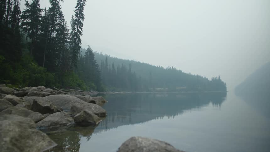 The water is calm in the lake under layer of smoke