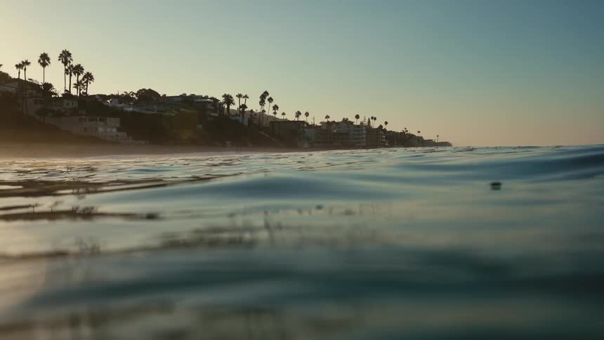 An ocean with water with trees buildings the sky and clouds in the background