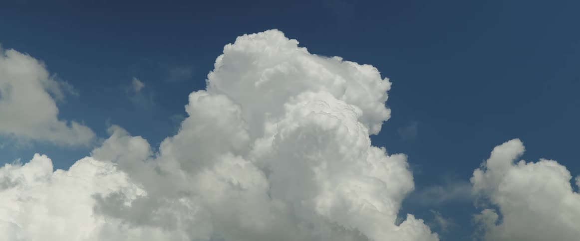 White puffy cumulus clouds float slowly across blue sky