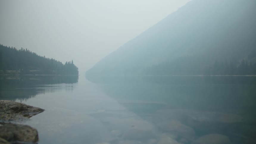 wildfire smoke over a calm lake near the mountains