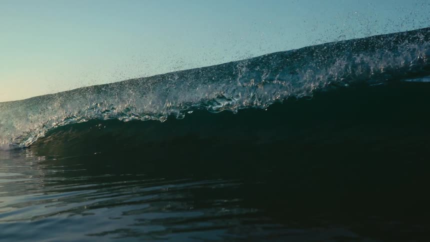 Sunlight is shining on an ocean wave as it is flowing and splashing over