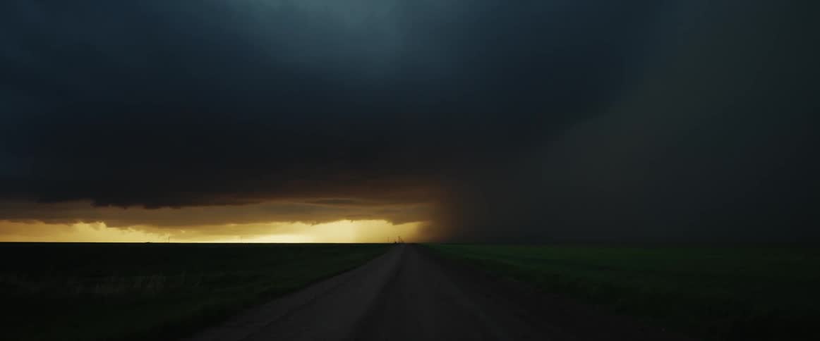Open road with darkness from a storm is overhead and sunlight at the end of the road