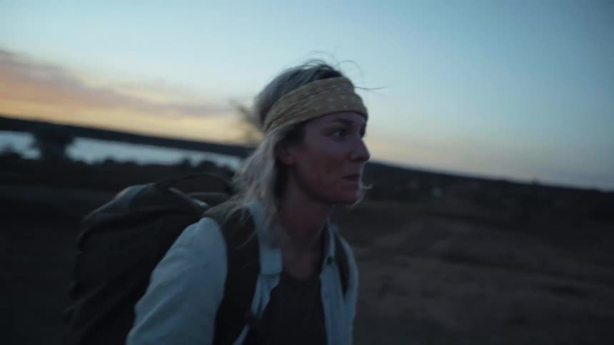 A woman with a backpack and a camera walking next to a vehicle with trees the sky and clouds in the background