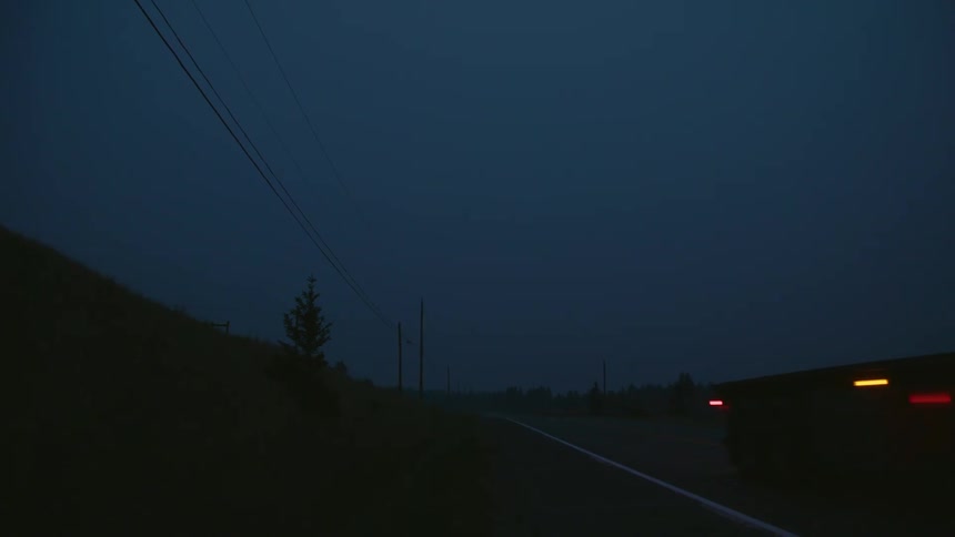 Semi truck drives down highway between forest and hills at night