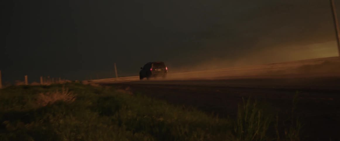 A landscape with a road and vehicle with the sky and clouds in the background