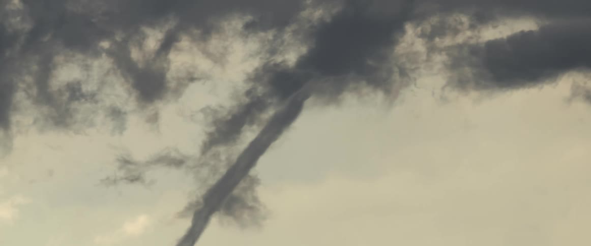 Thin rotating column of a breaking tornado touching ground over the plains