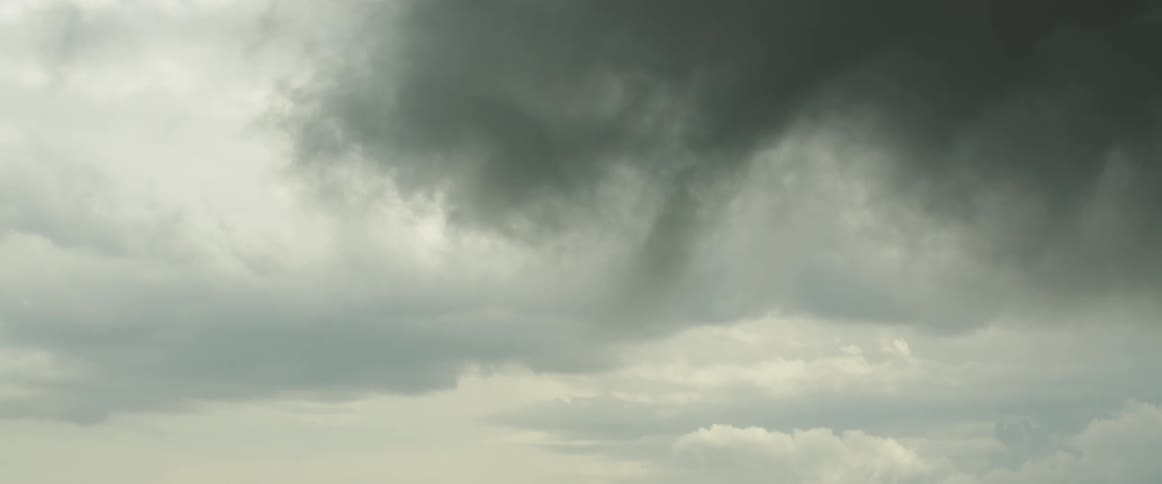 A funnel cloud is spinning from storm clouds during the day