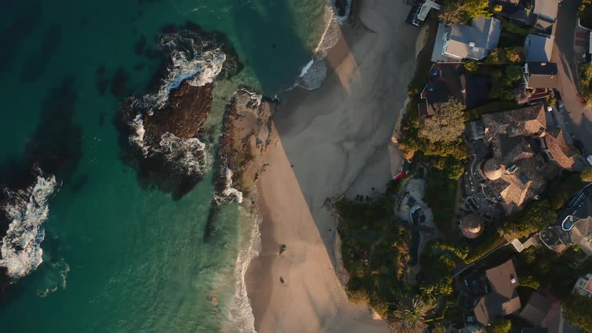 Sea waves crash onto the shore of a beach alongside a coastal neighborhood