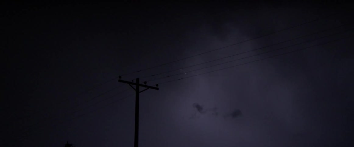 A utility pole and cables with lightning in the sky and clouds in the background