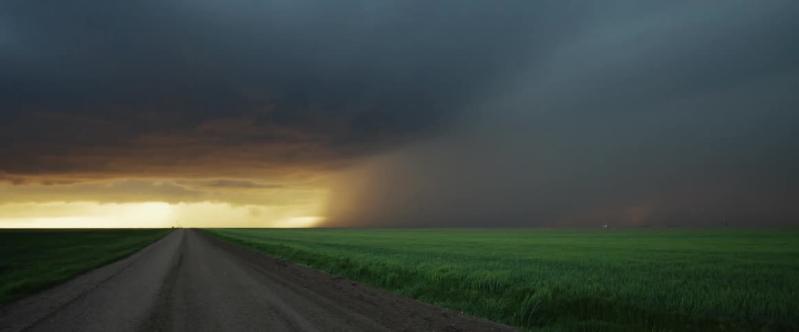 Rain pouring from dark storm clouds over the rural fields at sunset