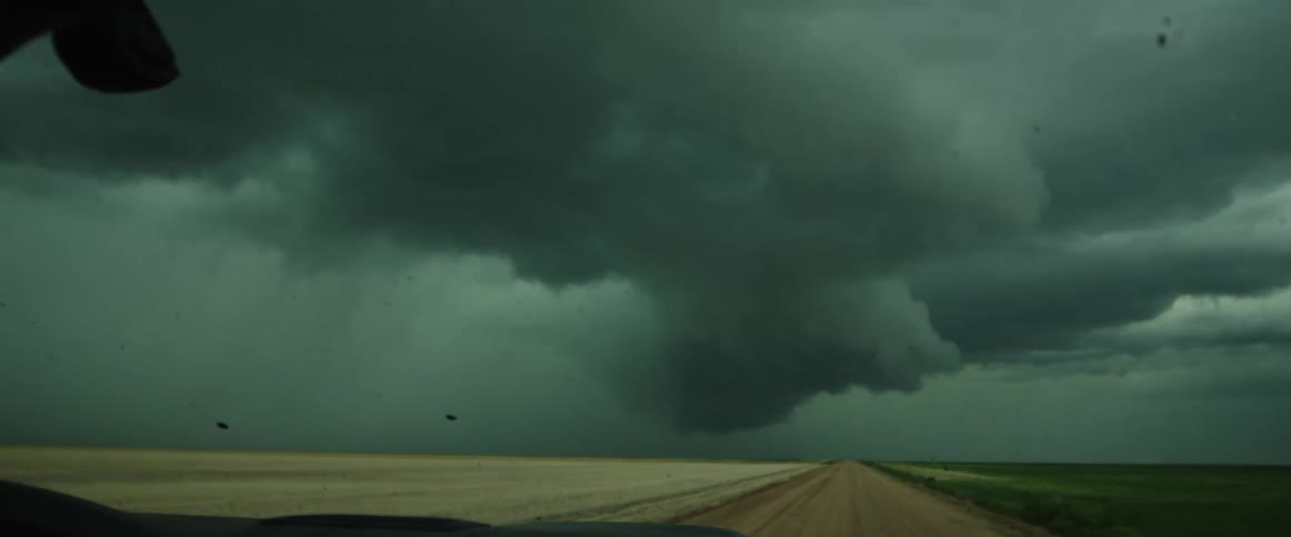 A dirt road with a vehicle with a storm the sky and clouds in the background