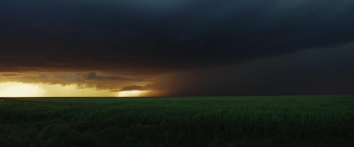 A landscape with a grassy field with the sky and clouds in the background
