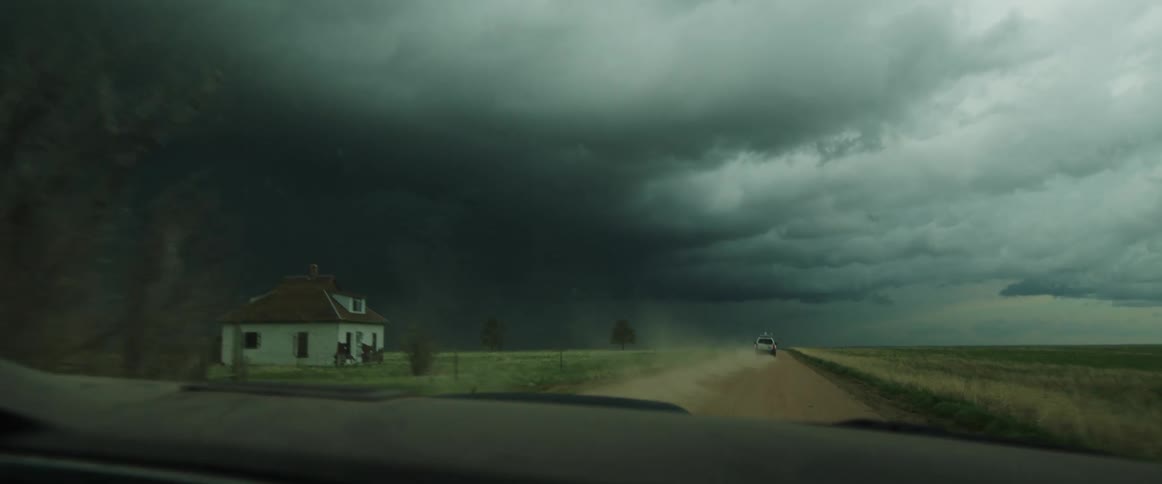 Storm chasers are on the move along a dirt road on farmland heading toward dark and looming storm clouds in the daytime