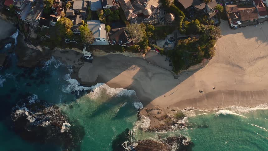 Aerial view of a seaside coastline with buildings along the shore as waves roll over the sand