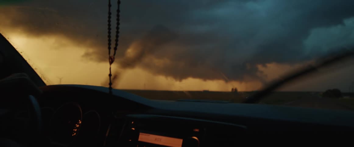 A man drives a car along a road through the countryside on a dark and stormy evening