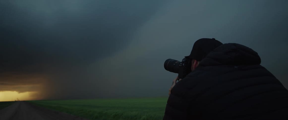 A man with a camera is photographing a lightening storm from a distance