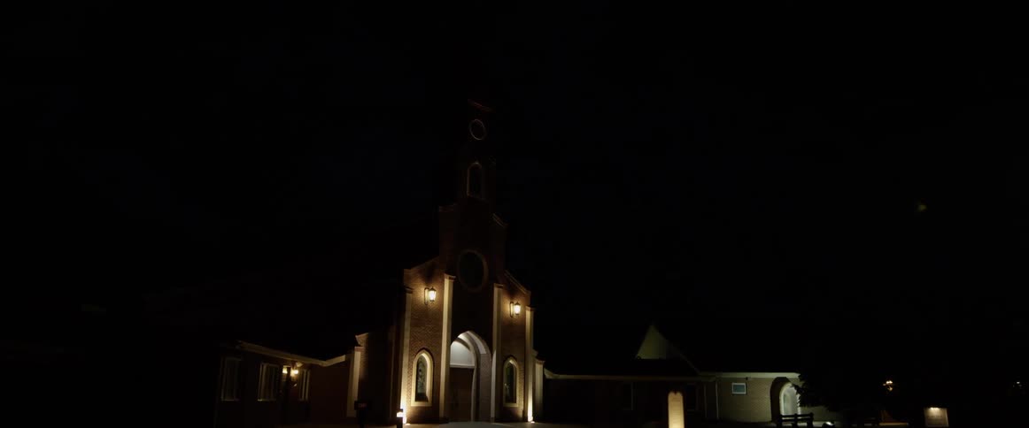 A church at night with an electrical storm in the background producing lightning flashes and streaks