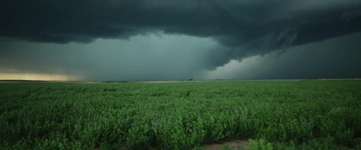 A landscape with a grassy field with a storm the sky and clouds in the background