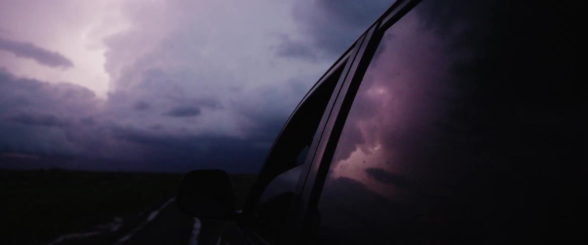 Lightning reflects on windows of parked car sitting on road