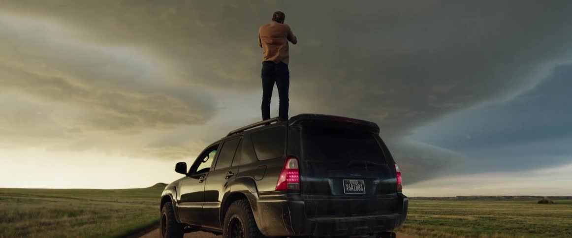 Man standing on the roof of a car parked on the road in the countryside takes pictures of clouds
