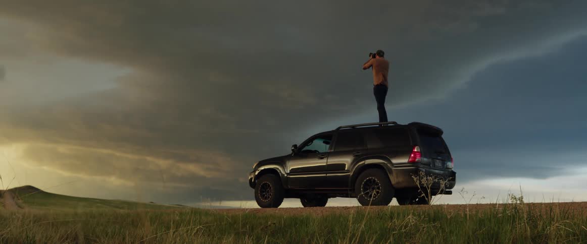 A man stands on the roof of his suv and takes photos of storm clouds