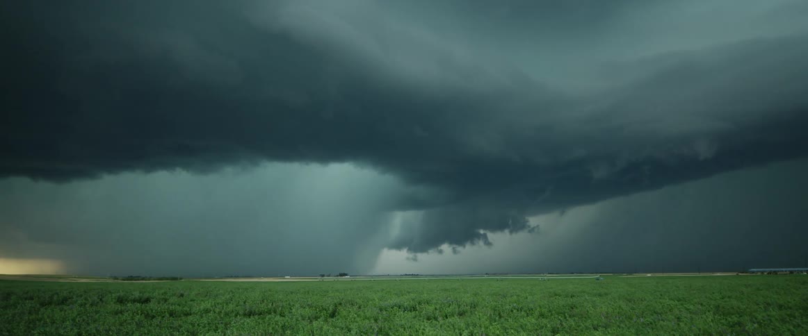 Dark storm clouds flow across plain past farm as traffic follows road