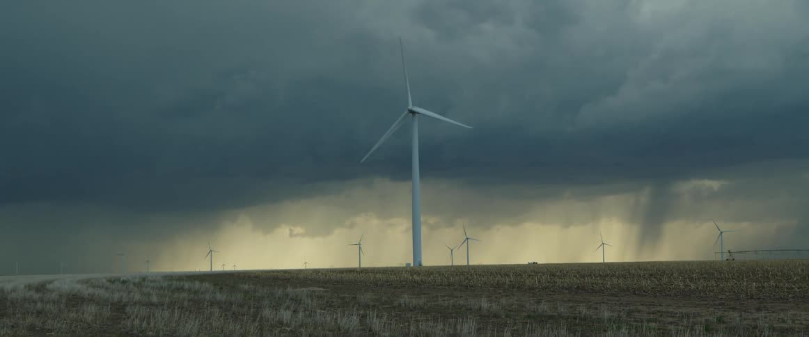Wind turbine on the field spinning under the dark storm clouds