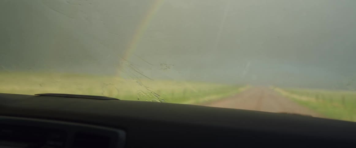 A vehicles windshield wipers run at full speed while driving down a narrow dirt road