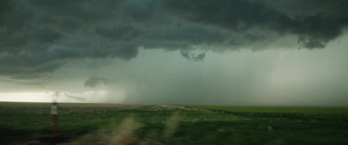 Passing by a storm chaser in a parked van watching a storm unfold over farmland during the day