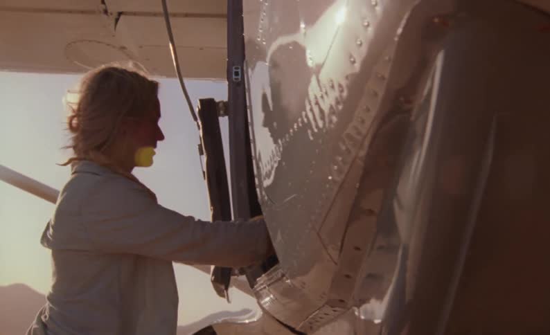 Woman carrying a backpack boards an airplane on a rural airfield at sunset