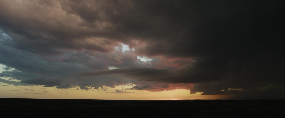 Sun glimmers on horizon in red sky as red tinted dark storm clouds shine with lightning