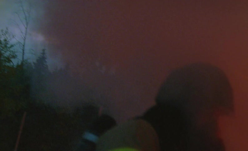 Firefighter maneuvers around burning vehicle at night spraying flames with hose