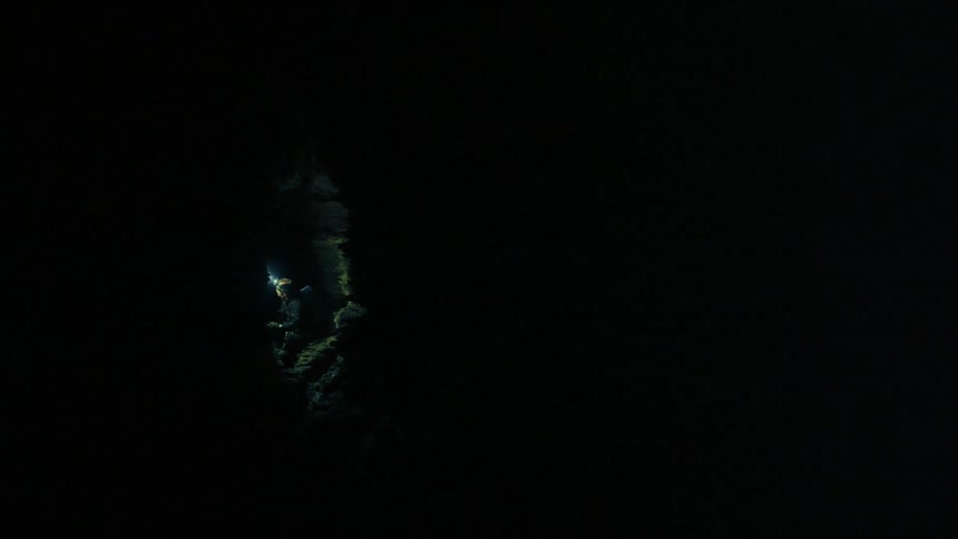 A flashlight shines through the entrance of a cave
