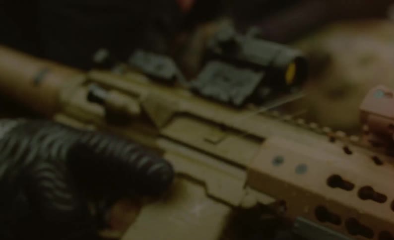 A soldier waits on the ground with his rifle in his hands on a rainy day