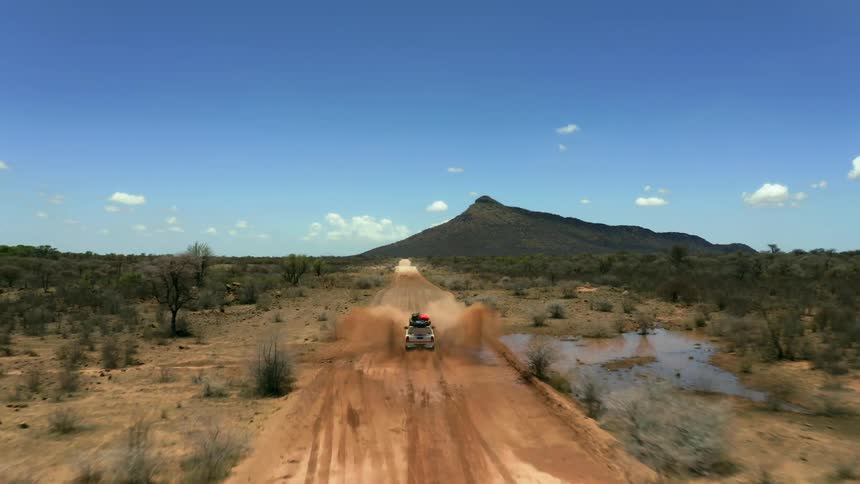 A sport utility vehicle drives through a large puddle while going down a dirt road in a canyon