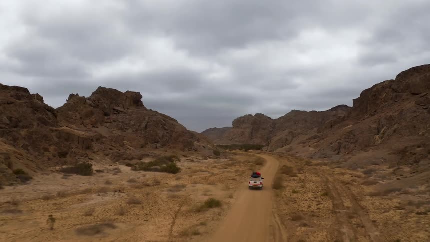 Car driving on a dirt road through a valley between the hills on the badlands