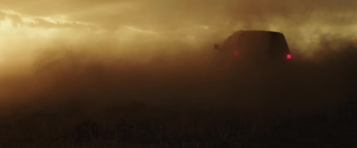 A vehicle kicks up a dust cloud as it drives in a circle in a field during the day