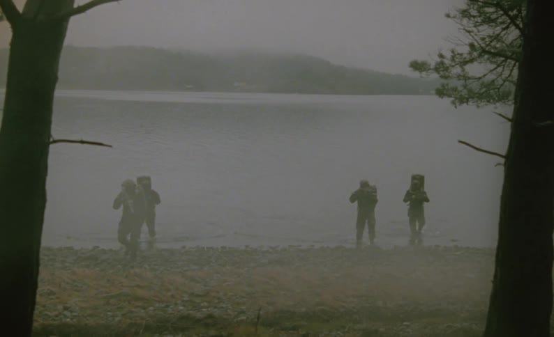 Soldiers walk out of a lake and toward a forest with guns drawn