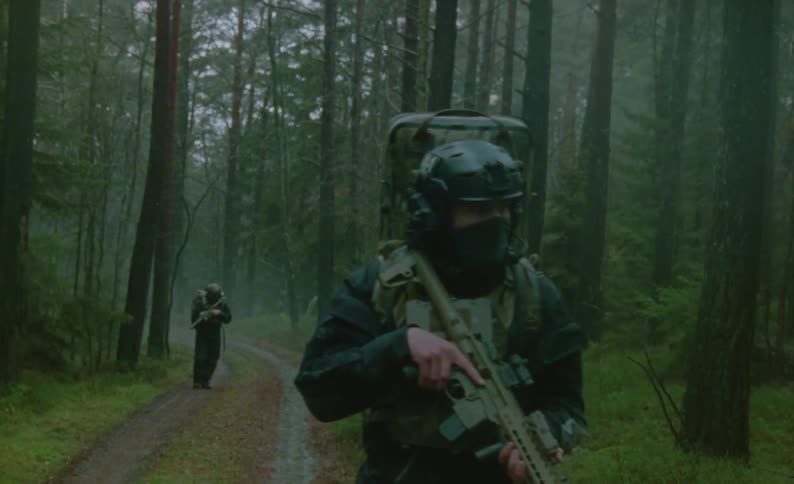 Two soliders walk through a forest with their guns drawn as they look around