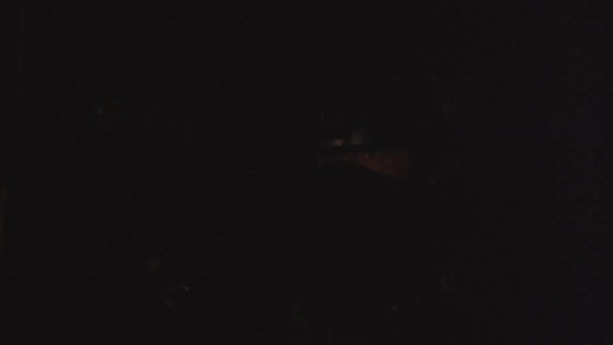 A soldier in black body armor scans a dark area with his firearm as a light slowly flashes nearby