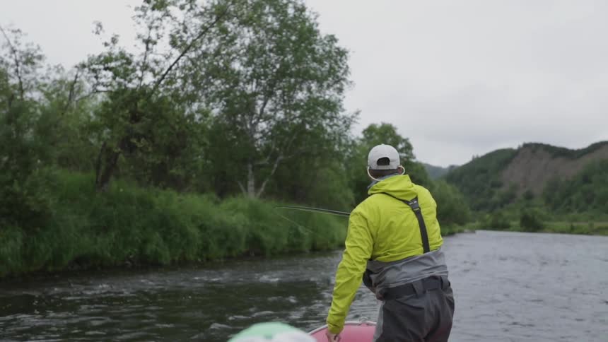 A fisherman standing up in a small boat pulls in his line