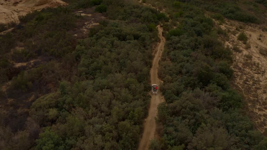 A vehicle drives down a dirt road through a forest to reach a remote canyon