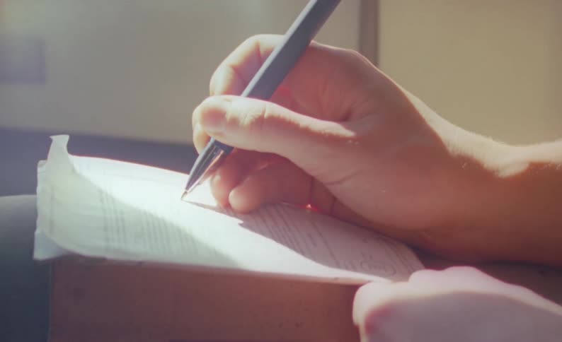 A hand is holding a pen and writing on paper